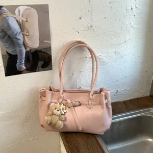 Pink soft leather tote bag with long handles and a cute teddy bear charm on wood desk