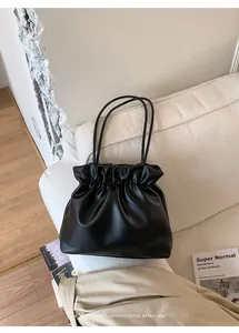 Detail of black pleated bucket tote bag with matte leather texture on a minimal sofa