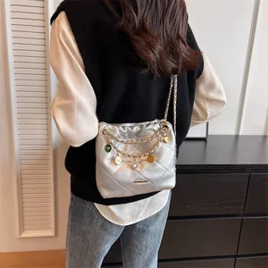 Sac seau argenté matelassé avec chaîne et breloques colorées porté par un mannequin