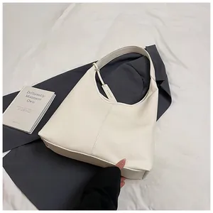 Détail d'un sac cabas blanc en cuir à motif litchi avec étiquette sur un blazer gris