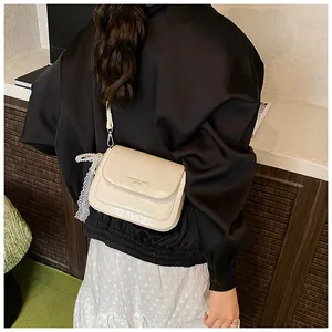 Detail of cream crossbody bag with lace bow charm and textured pebble leather finish