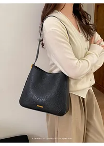 Détail du cuir grainé noir et des ferrures dorées d'un sac seau au style rétro épuré