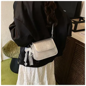 Detail of silver crinkled texture crossbody bag with white lace bow charm accessory