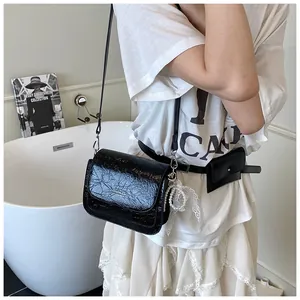 Close-up of black glossy crossbody bag featuring pleated texture and elegant pearl charms