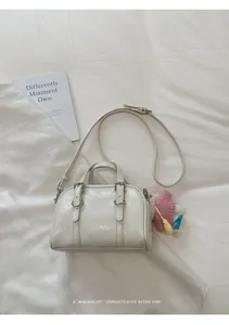 Dettaglio borsa Boston crema con cinturini in pelle e ciondolo bambola in maglia rosa