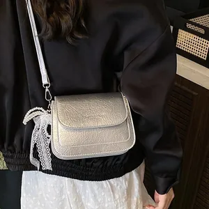 Silver metallic crossbody mini bag with pearl bow detail and lace charm on model