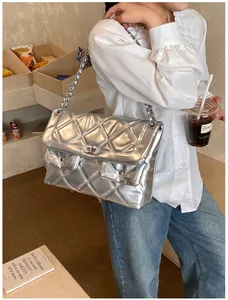 Detail of silver quilted chain bag with metallic finish and rhinestone lock on model