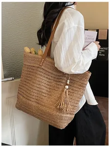 Borsa tote in paglia con manici in pelle marrone e nappina decorativa in un ambiente casual