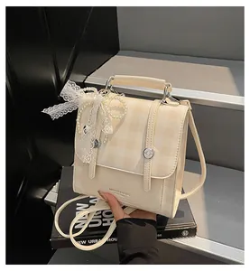 Detalle del bolso de cuadros crema con colgante de lazo de perlas sobre fondo de libro