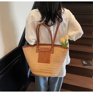 Detail of a woven straw tote bag with brown leather straps shown on a model