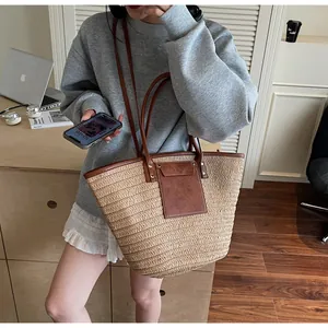 Close-up of large woven tote bag with beige straw texture and dark brown leather trim