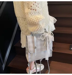 Detalle del bolso bandolera plateado a cuadros con lazo de encaje y cadena de perlas