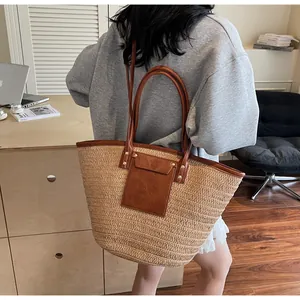 Detail of hand-woven straw tote bag with brown faux leather trim and metallic rivets