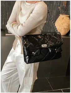Detail of black patent leather crossbody bag with quilted pattern and metal chain