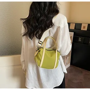 Detail of green canvas crossbody bag with beige strap shown in a casual lifestyle setting