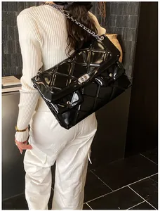 Detail of a large black quilted messenger bag with glossy finish and chain strap worn by model