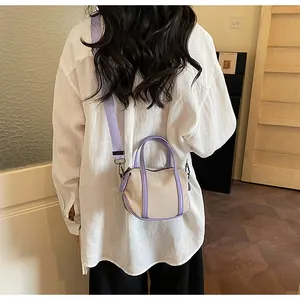 Detailed back view of a mini beige canvas crossbody bag with purple handles on a model