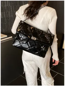 Detail of glossy black quilted chain bag with silver hardware on model's shoulder