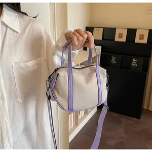 Close-up of cream canvas mini Boston bag with purple leather straps and metal hardware