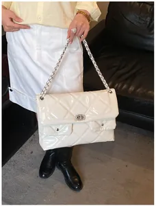 Close-up of white quilted patent leather bag with silver chain strap and rhinestone lock
