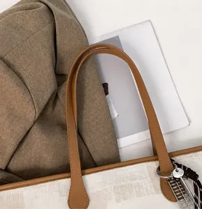 Detail of canvas tote bag with brown leather handles and decorative metal abacus charm