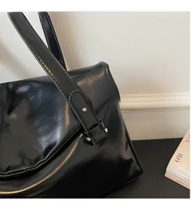 Close-up of shiny black PU leather shoulder bag with glossy finish and silver metal rivets