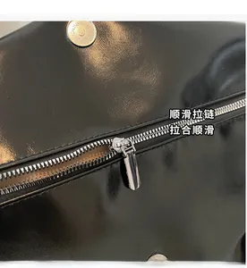 Close-up of premium black glossy leather tote bag with silver metal zipper and hardware