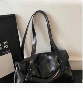 Detail of high-gloss black tote bag showing durable long handles and side buckle accent