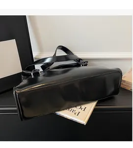 Detail of a black glossy leather tote bag with a smooth finish and sturdy top handles