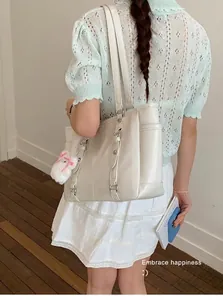 Detail of off-white tote bag with vertical straps and plush bunny charm on a model