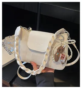 Detail of cream crossbody bag featuring woven texture and plush horse charm accessory