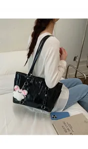 Glossy black patent leather tote bag with silver buckles and a white plush bear charm