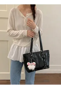 Detailed view of a black glossy tote bag with dual straps and a plush bunny charm