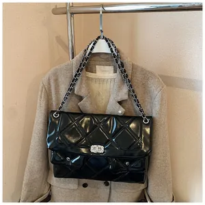 Detail of glossy quilted crossbody bag with silver twist lock and chain strap on a blazer