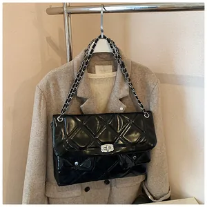 Detail of black quilted crossbody bag with silver chain strap on beige tweed jacket
