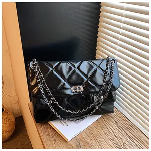 Detail of black quilted patent leather bag with sparkling rhinestone buckle and chain strap