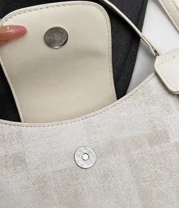 Detail of metal magnetic clasp on a textured cream crossbody bag with geometric patterns
