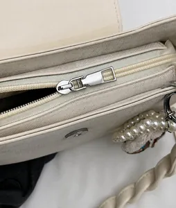 Close-up of smooth hardware zipper and beaded pearl pendant on beige crossbody bag