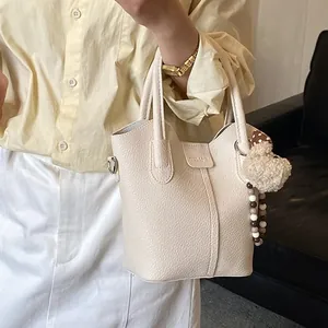 Creamy white litchi leather bucket bag with plush bear charm and crossbody strap