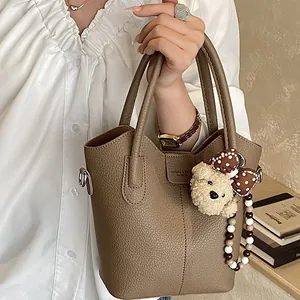 Brown litchi grain bucket bag with teddy bear charm and dual handles shown by model