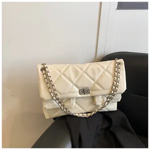Detail of quilted beige chain bag with silver twist lock on leather background