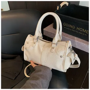 Close-up of beige lychee grain leather pillow bag with silver studs and dual handles