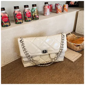 Close-up of quilted cream leather texture and metal chain strap on a small square bag
