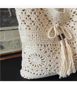 Close-up of beige crochet knit bag featuring floral patterns, wood beads, and tassels