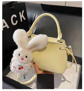 Detail of soft yellow faux leather handbag with cute plush rabbit charm and crossbody strap