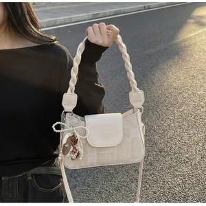 Detail of oat-colored crossbody bag with woven handle, canvas texture, and cute bear charm