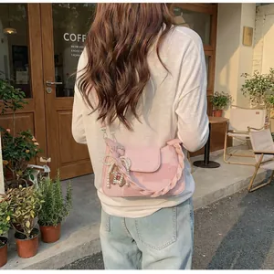 Close-up of pink crossbody bag with woven handle, pearl bow and charm details