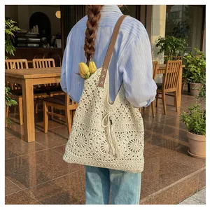 Detail of crochet tote bag with openwork pattern, tassel charm and leather shoulder strap