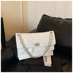 Detailed view of white quilted patent leather bag with silver chain strap on leather sofa