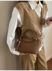 Close-up of brown textured bucket bag with detailed quilting, tassels and logo detail